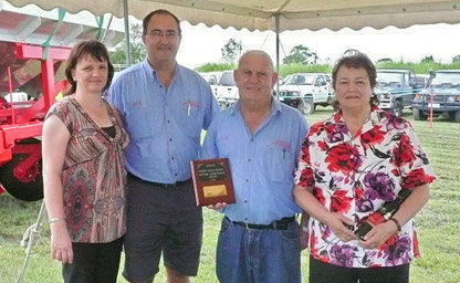 Four people posing, man in middle holding Lifetime Achievement Award